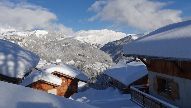 A wooden cabin with snow-covered roofs, surrounded by a mountainous landscape.