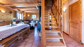 A wooden interior with a staircase, a dining area with a table and benches, and a sofa.
