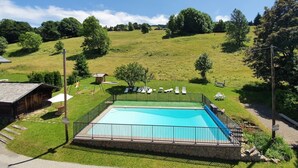 A rectangular swimming pool with a black metal fence, surrounded by a grassy area with lounge chairs.