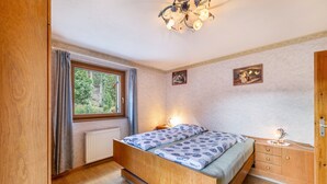 Een slaapkamer met een houten bed, nachtkastje, dressoir, raam met gordijnen en een kroonluchter.
