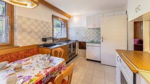 Een compacte keuken met een eettafel, stoelen, een koelkast en een raam met uitzicht.