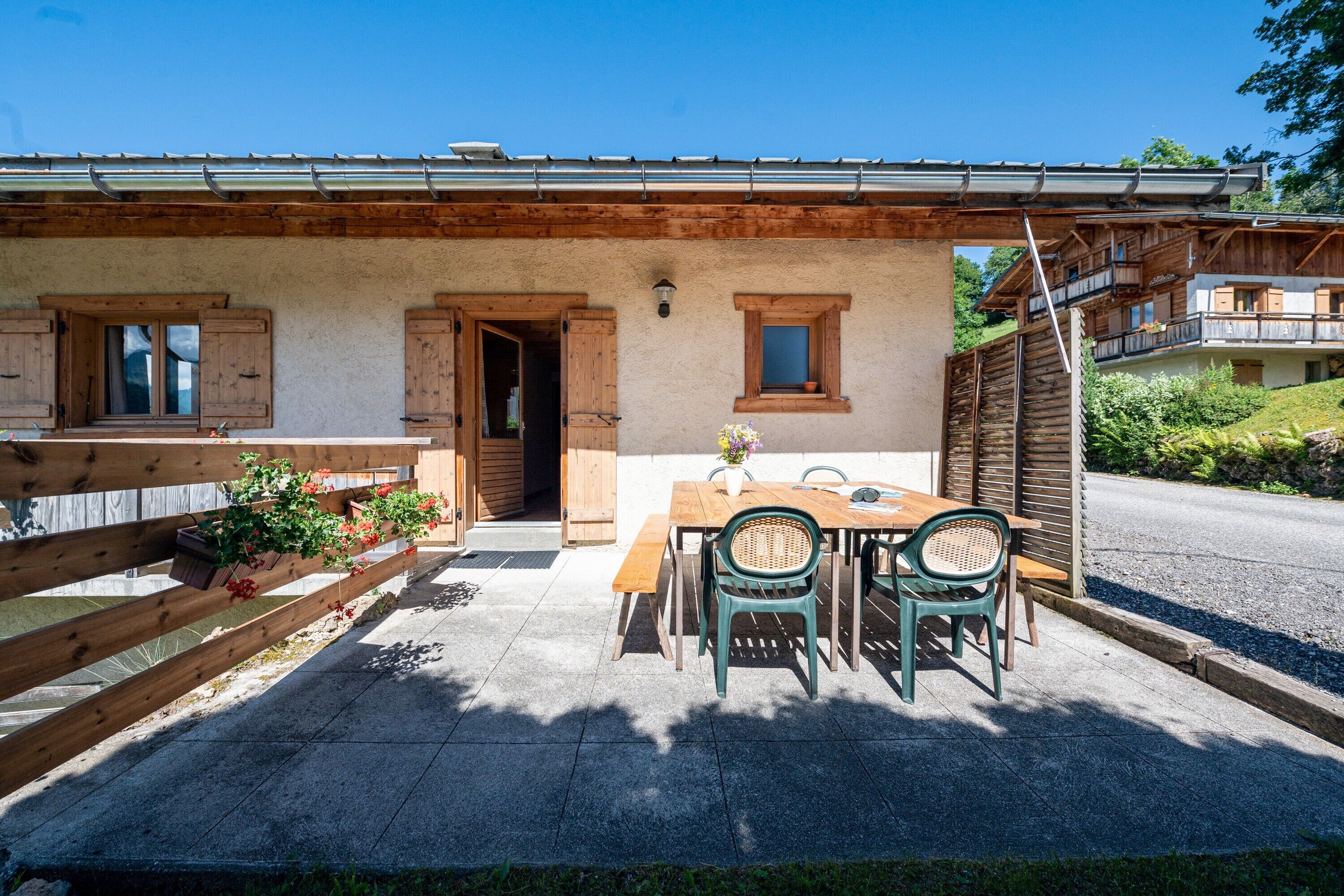 Una cabaña rústica con fachada de madera, un patio con mesa y sillas, y una valla de madera.
