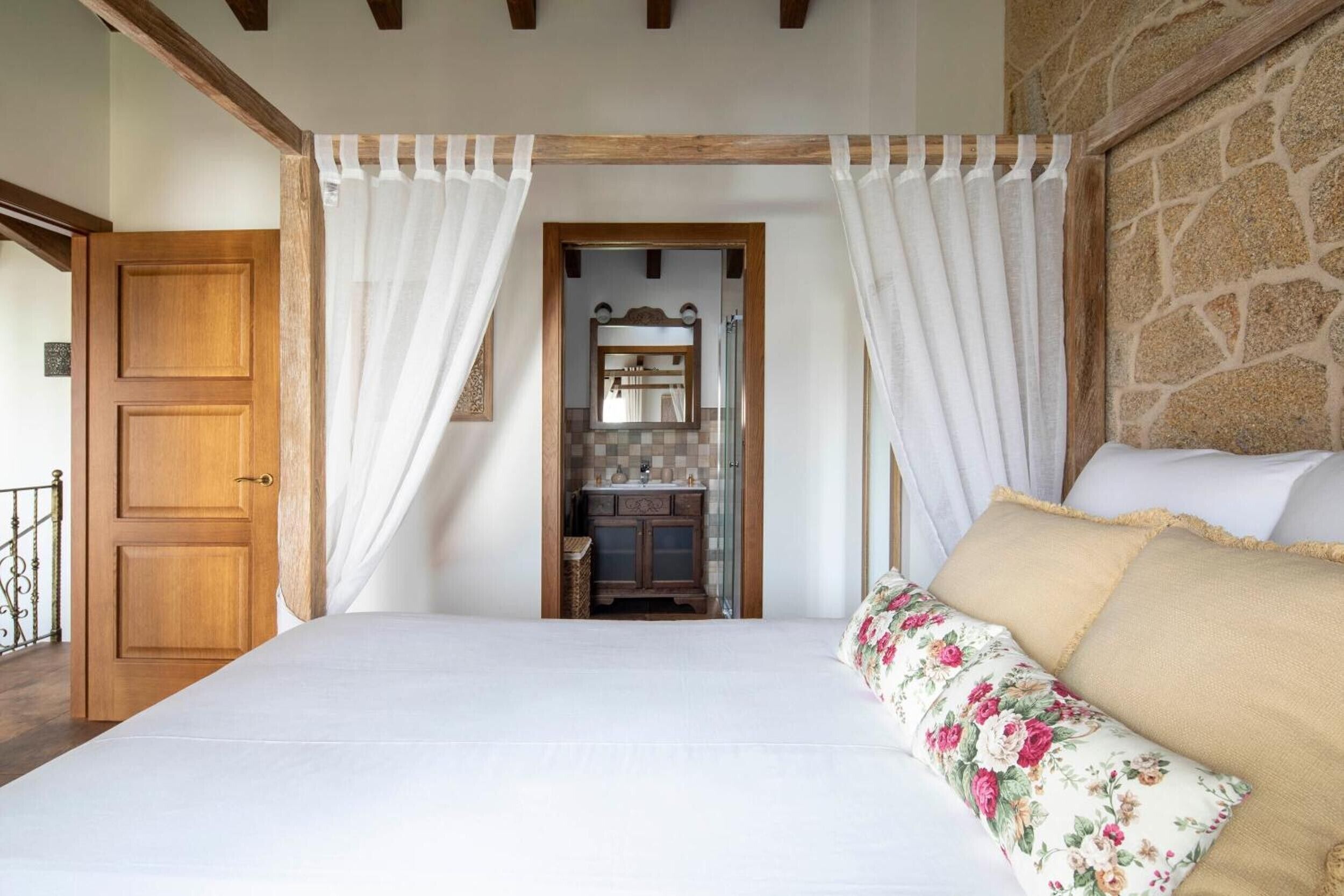 Une chambre à coucher avec un lit, une porte en bois, un mur en pierre et une salle de bain visible à travers une porte.