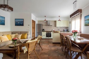 Una cocina moderna con una isla central, comedor con sillas de mimbre y un sofá con cojines.