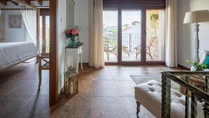 A room with a bed, a small table with a vase, a chair, a lamp, and a balcony with wicker furniture. - Holiday Home 'Fogar Da Roda' with Private Terrace, Balcony and Wi-Fi (Vilagarcia de Arousa)