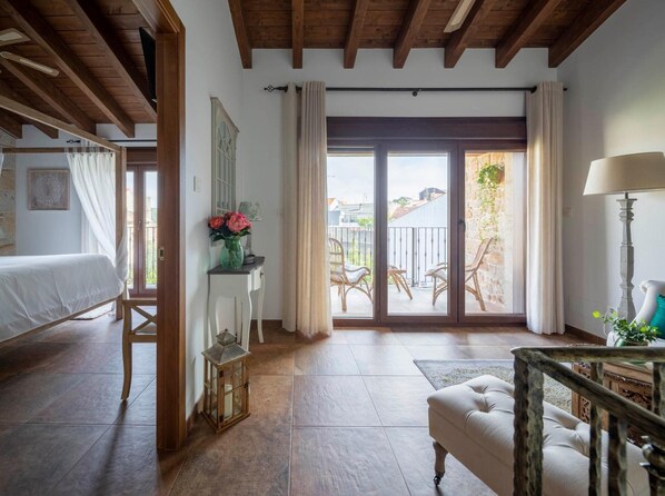 A room with a bed, a small table with a vase, a chair, a lamp, and a balcony with wicker furniture. - Holiday Home 'Fogar Da Roda' with Private Terrace, Balcony and Wi-Fi (Vilagarcia de Arousa)
