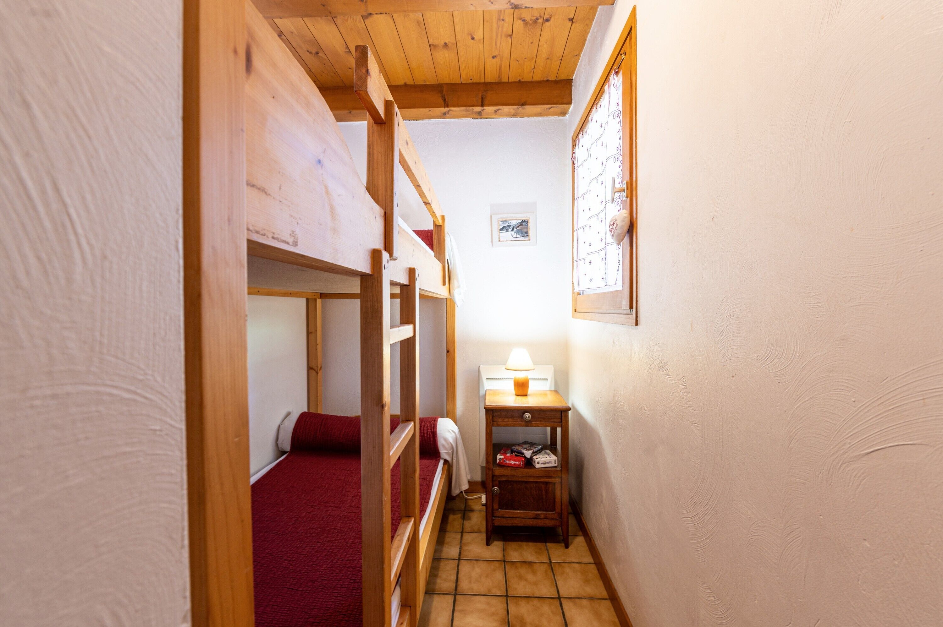 Un couloir étroit avec des lits superposés en bois, une petite table avec une lampe et une carte encadrée accrochée au mur.