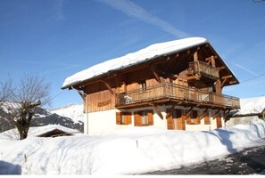 A wooden chalet with a balcony, surrounded by snow-covered mountains.