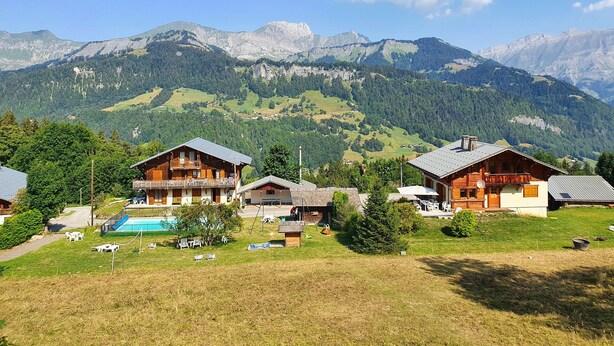A mountain resort with wooden cabins, a swimming pool, and expansive views of the surrounding mountains. - Apartment 'L'Hermine, Piscine Et Aire De Jeux' with Mountain View, Private Terrace and Wi-Fi (Crest-Voland)