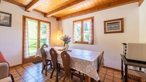 A dining area with a table, chairs, a vase with flowers, and a television on a stand. - Apartment 'L'Hermine, Piscine Et Aire De Jeux' with Mountain View, Private Terrace and Wi-Fi (Crest-Voland)