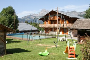 A wooden cabin with a balcony, a swing set, and a small pool.