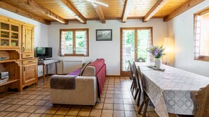 A room with a wooden ceiling, a sofa, a dining table with chairs, a TV, and a window with curtains. - Apartment 'L'Hermine, Piscine Et Aire De Jeux' with Mountain View, Private Terrace and Wi-Fi (Crest-Voland)