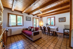 A cozy living room with a sofa, dining table, chairs, and wooden beams on the ceiling.