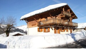 A wooden chalet with a balcony, surrounded by snow-covered mountains. - Apartment 'L'Hermine, Piscine Et Aire De Jeux' with Mountain View, Private Terrace and Wi-Fi (Crest-Voland)