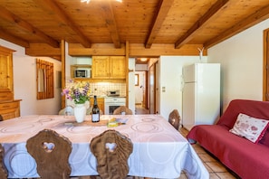 A wooden interior with a dining table, chairs, a sofa, and a kitchen area.