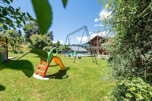 Un terrain de jeux avec des balançoires et des toboggans, entouré de verdure et avec un bâtiment en arrière-plan.