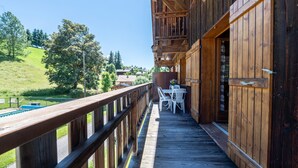Une terrasse en bois avec une rambarde, une table entourée de chaises et une vue sur un paysage verdoyant.