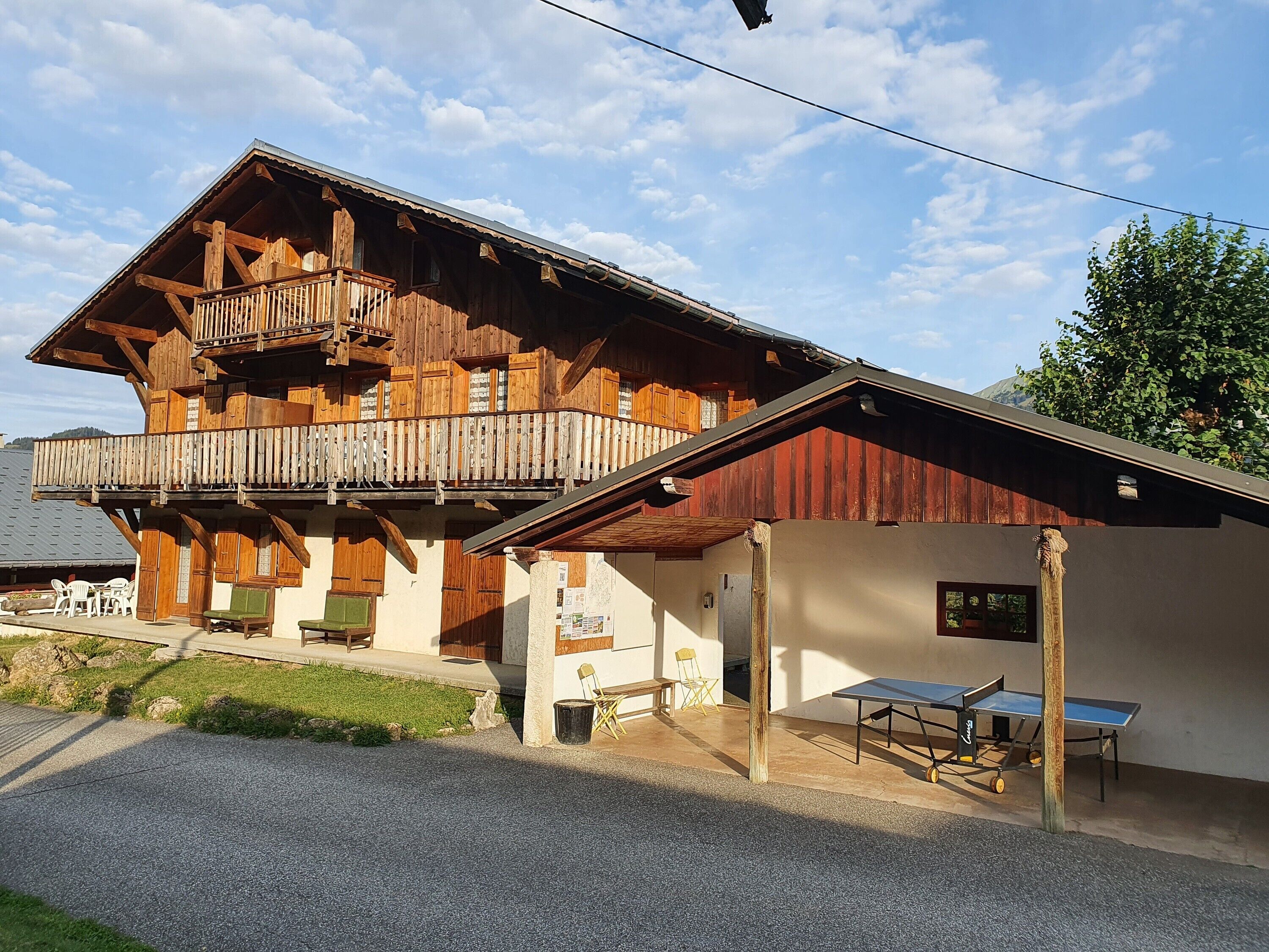 Een houten chalet met een balkon, buitenmeubels en een tafeltennistafel.