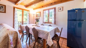 Een eethoek met een tafel voor zes personen, houten stoelen, een koelkast en een raam met gordijnen.