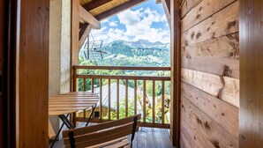 Een houten balkon met een tafel en bankje, met uitzicht op een bergachtig landschap.