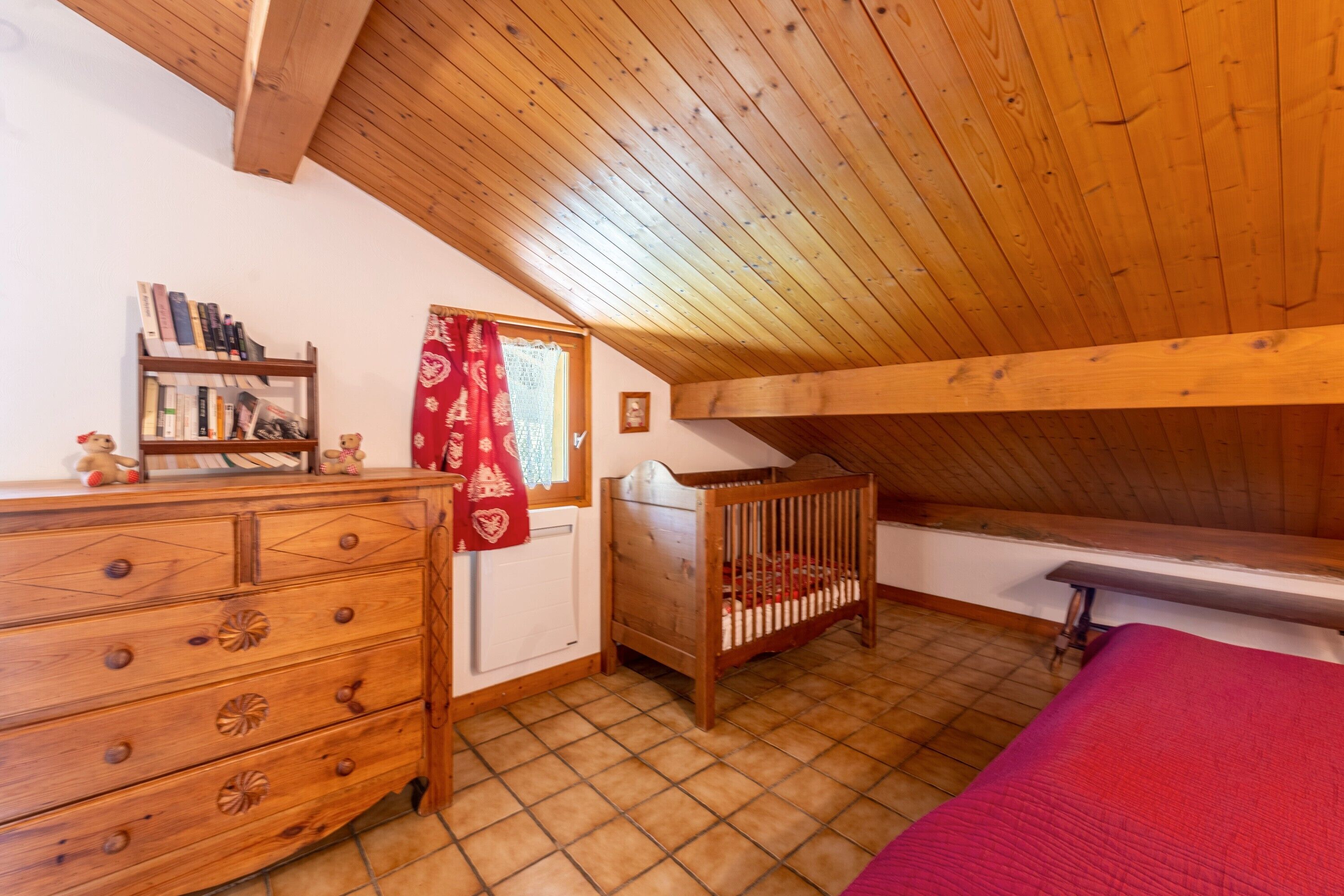 Una habitación con techo de madera, una cuna, un aparador y una ventana con cortina.