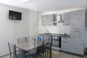 A modern kitchen with grey cabinets, a built-in oven, and a flat-screen TV mounted on the wall. - Homiday - Tulip Residence, Three-Room Apartment (Scerne)