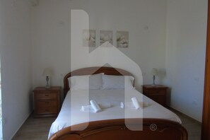 Un lit bien fait, avec du linge de lit blanc et des serviettes pliées, deux tables de chevet avec des lampes et trois œuvres d’art accrochées au mur.