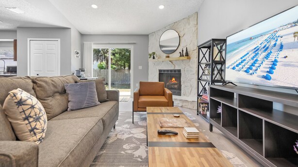 Ein modernes Wohnzimmer mit Sofa, Couchtisch, Kamin und einem großen Fernseher, der eine Strandansicht zeigt.