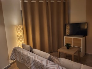 A living room with a sofa, a TV on a stand, a lamp, and a curtain.
