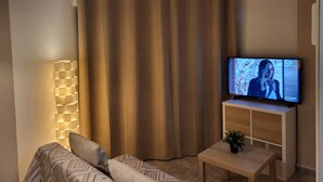A living room with a television, a sofa, a lamp, and a small table with a plant.