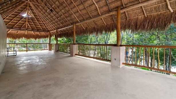 A covered outdoor area with a concrete floor, wooden railing, and a thatched roof. - Encanto Private Balcony 2 Pools 5 Minutes To Beach (Tulum)