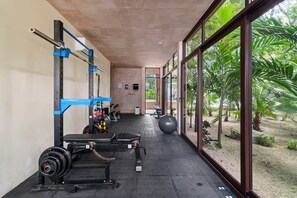 Ein Fitnessraum mit Gewichthebern, einer Bank und einem großen Fenster mit Blick auf Grünflächen.