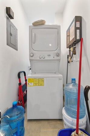 A compact laundry room with a front-loading washing machine, a water heater, and a large water dispenser.