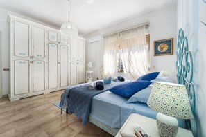 Ein Schlafzimmer mit Bett, Nachttisch, Lampe, Kleiderschrank und einem Fenster mit Vorhängen.