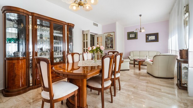 Ein Essbereich mit Holztisch und Stühlen, eine Glasschrank mit Dekoration und ein Wohnzimmer mit Sofa und Lampe.