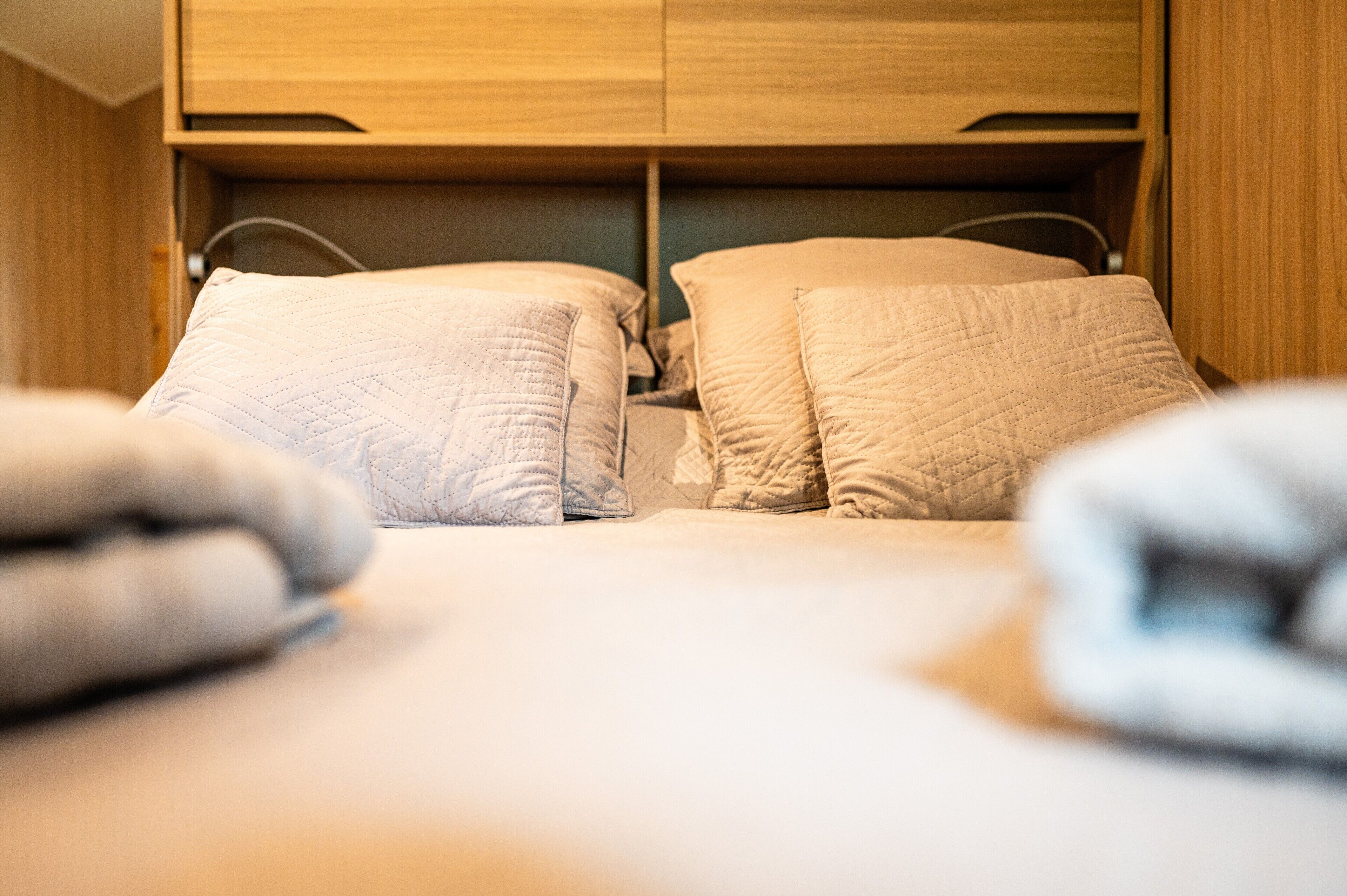 A bed with a quilted headboard and pillows, a wooden wardrobe, and a visible cable.