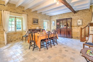 Une pièce aux murs de pierre, comprenant une table à manger, des chaises, un buffet et un escalier.