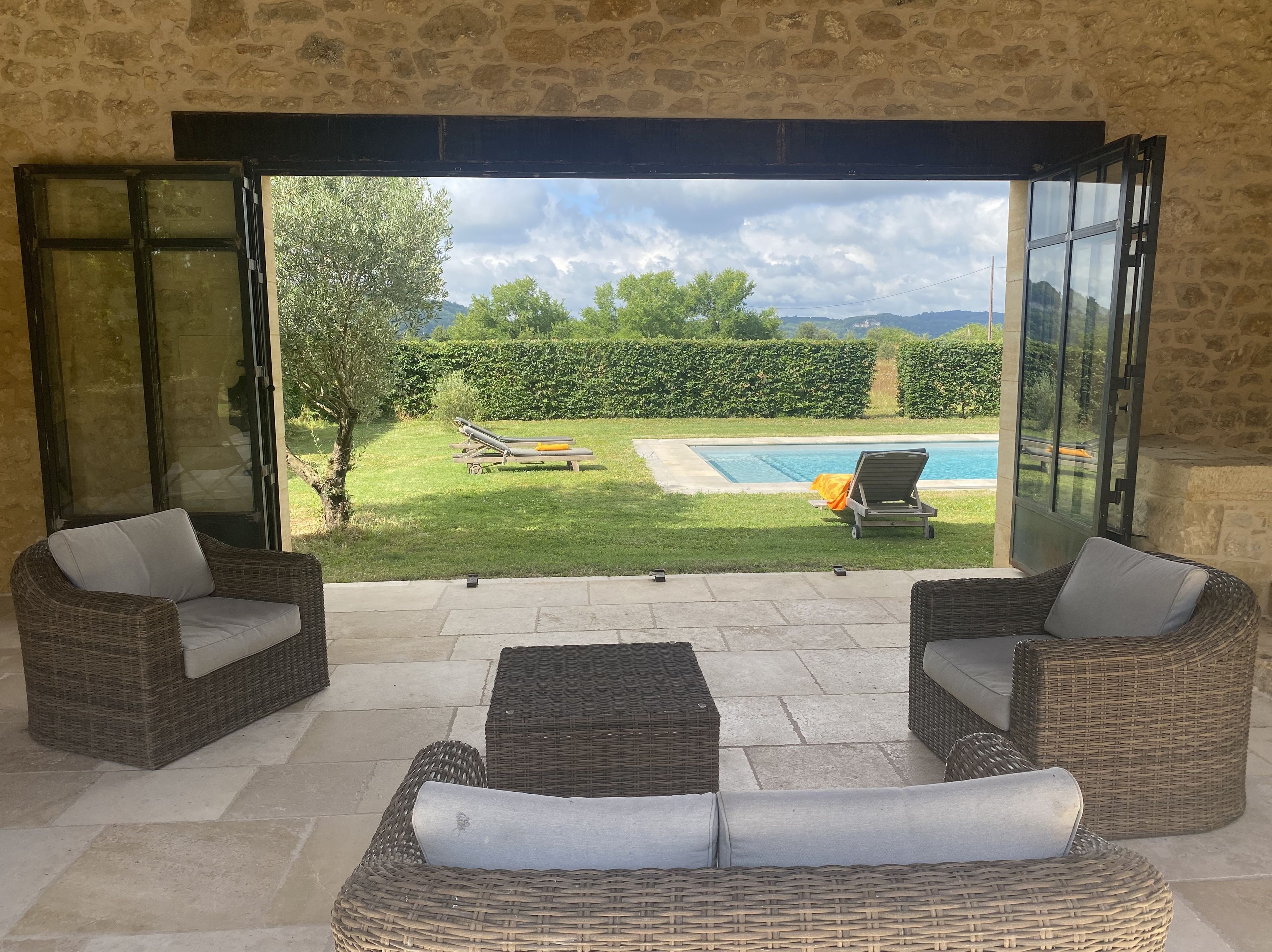 Une terrasse ouverte, meublée de mobilier en osier, avec une piscine et une vue sur un paysage verdoyant.