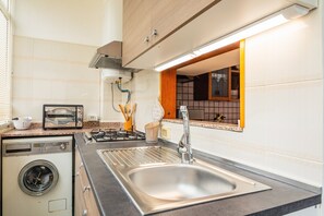 A kitchen with a stainless steel sink, a built-in washing machine, a toaster, and a window with a view.