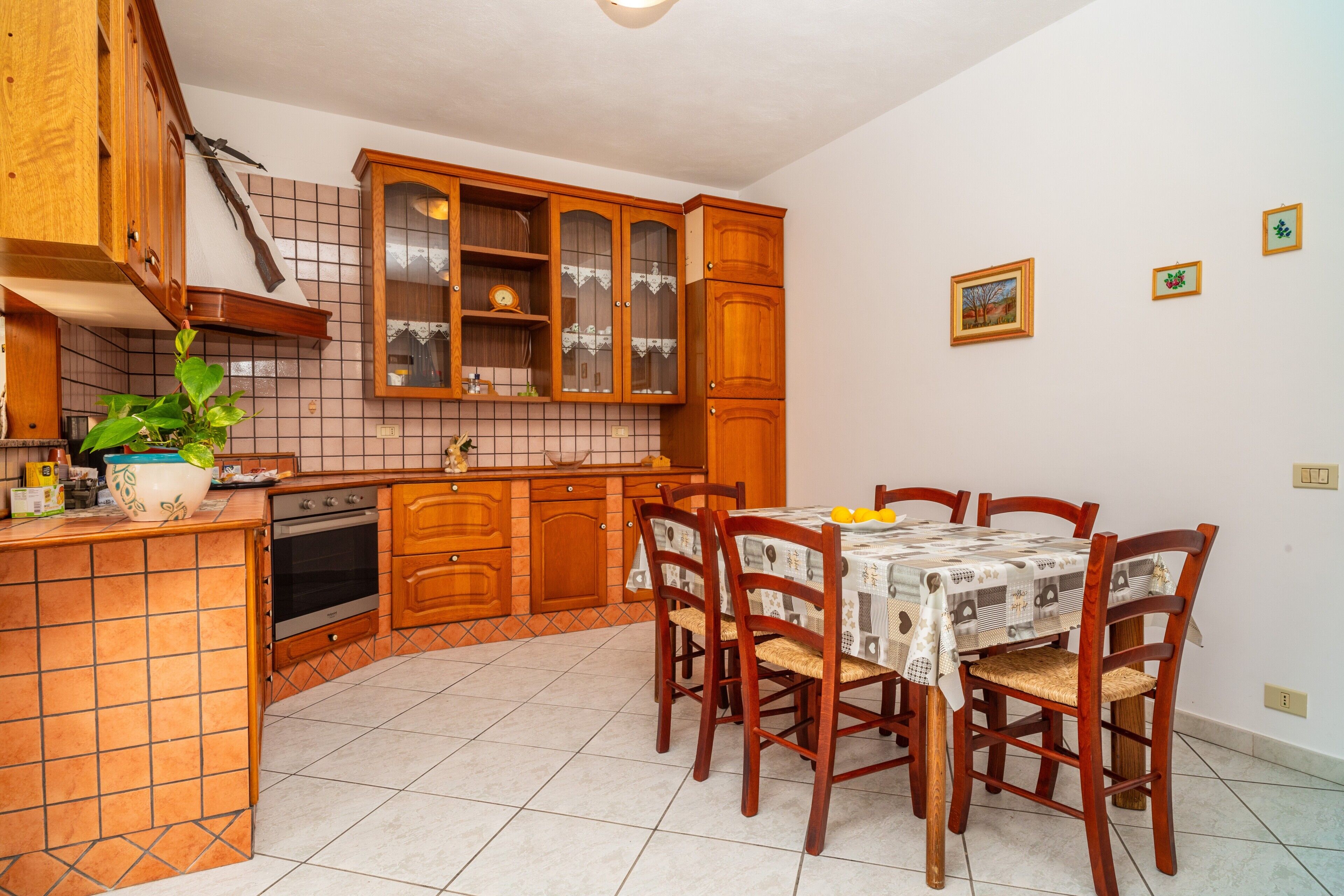 A kitchen with wooden cabinets, a tiled backsplash, a dining table with chairs, and a potted plant.