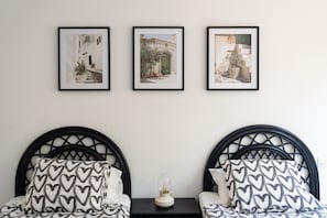 Una habitación con dos camas, una mesita pequeña y tres cuadros en la pared.