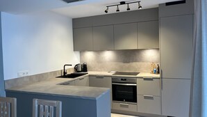 A modern kitchen with grey cabinets, a built-in oven, a kettle, and a sink.