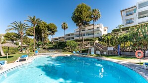 A swimming pool with lounge chairs, palm trees, and a building with balconies.