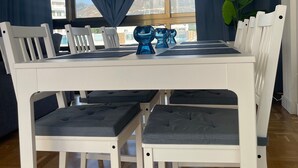 Un coin repas avec une table blanche, des rideaux bleus et une vue sur les bâtiments.