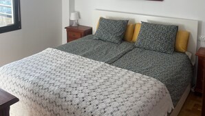 Une chambre à coucher comprenant un lit, une table de chevet, une lampe, un tableau encadré accroché au mur et un ventilateur de plafond.