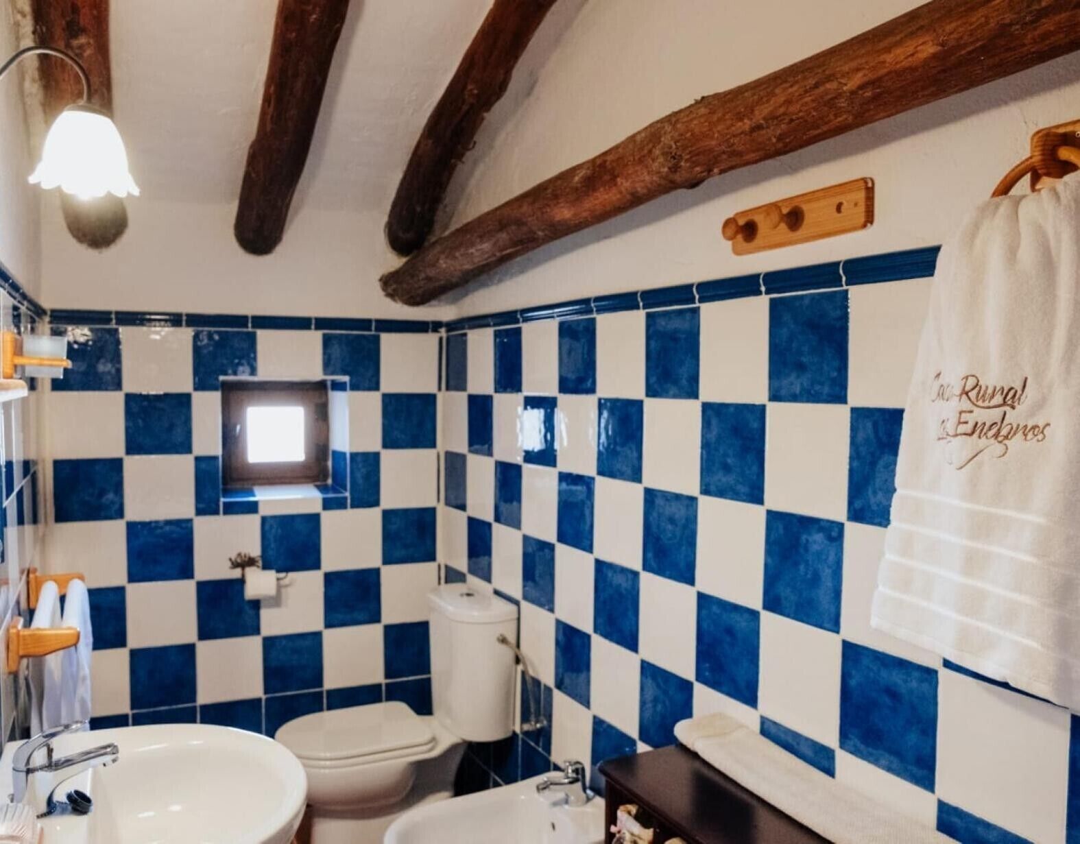 A bathroom with a checkered blue and white tile wall, a white sink, a toilet, and a towel hanging on the wall.