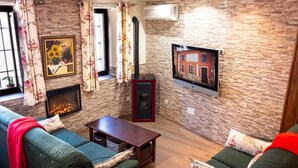 A living room with a fireplace, a television mounted on the wall, and a sofa. - Holiday Home 'Casa Rural Los Enebros' with Private Pool, Wi-Fi and Air Conditioning (Los Navalucillos)