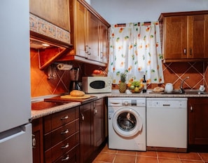 Una cocina compacta con armarios de madera, un microondas, una lavadora y un frutero sobre la encimera.