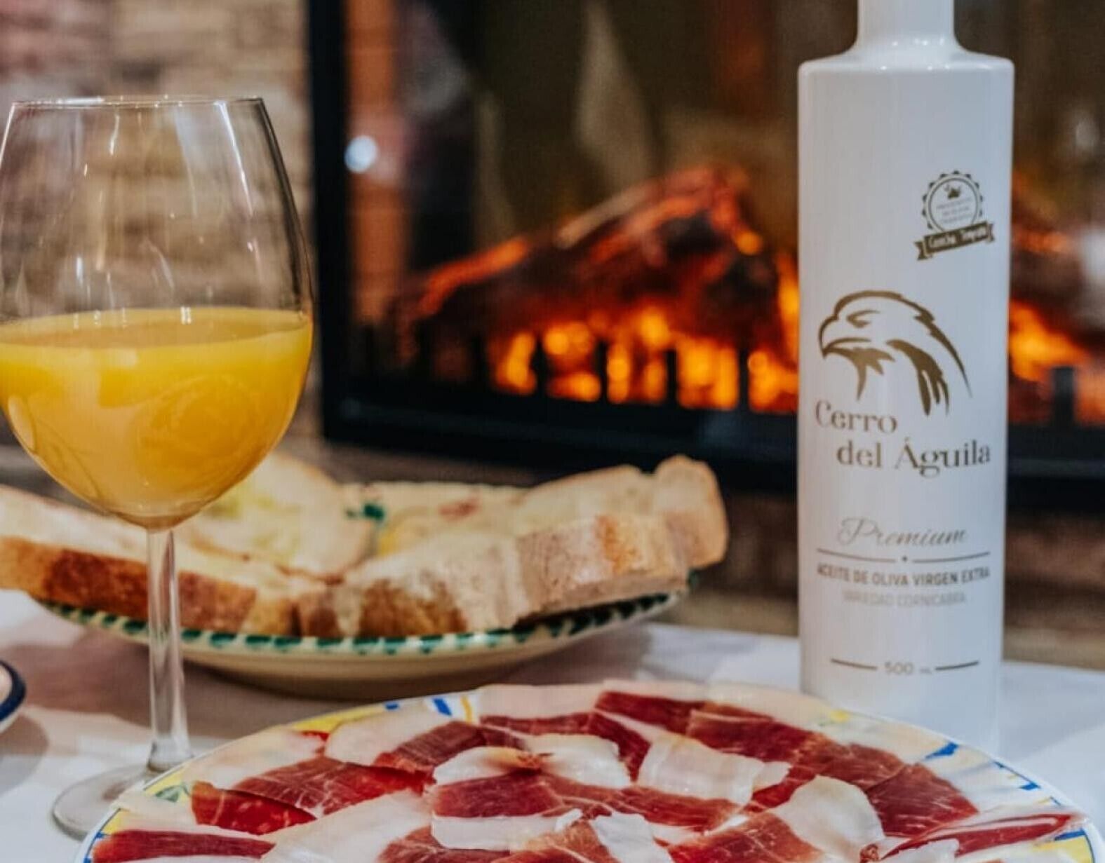 Un vaso de zumo de naranja, una botella de aceite de oliva premium Cervo del Águila, y un plato de embutidos curados.