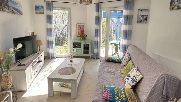 Ein Wohnzimmer mit einer Couch, einem Fernseher, einem Couchtisch und Blick durch große Fenster.